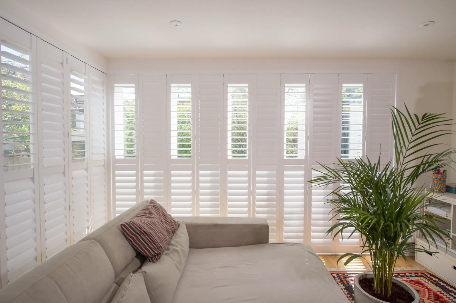 Tracked bi-folding shutters running across a wide opening in a Suffolk living room
